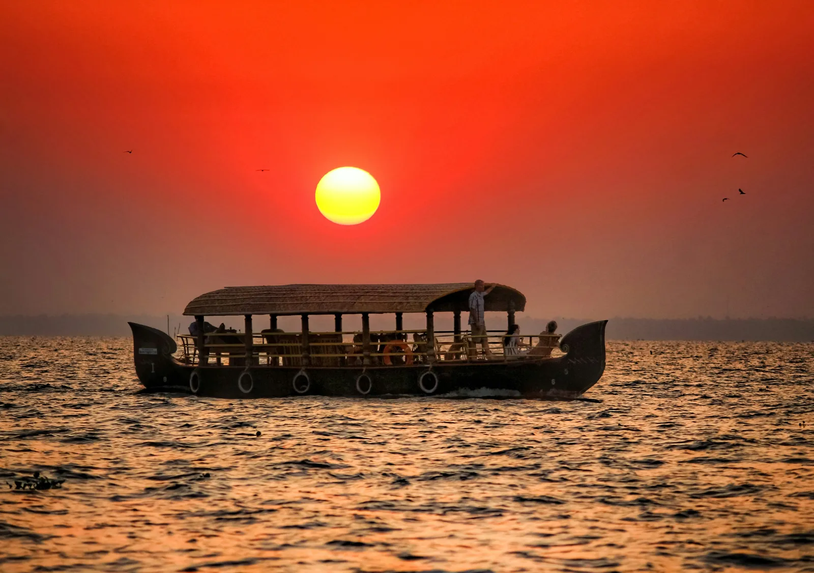 Canopied country boat cruising Vembanad Lake beneath a fiery sunset at Kumarakom
